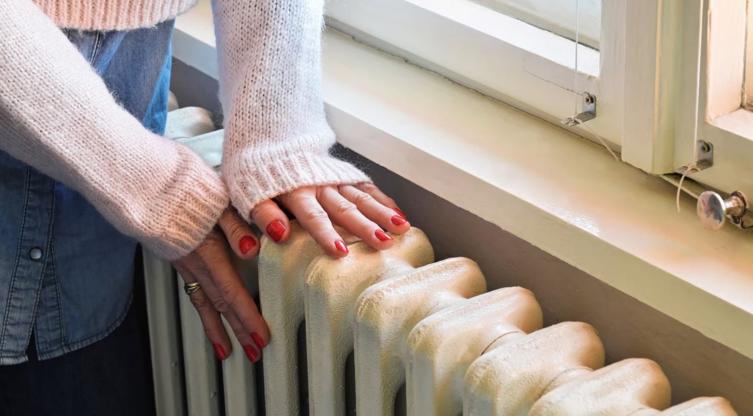 Женщина греет руки на батарее