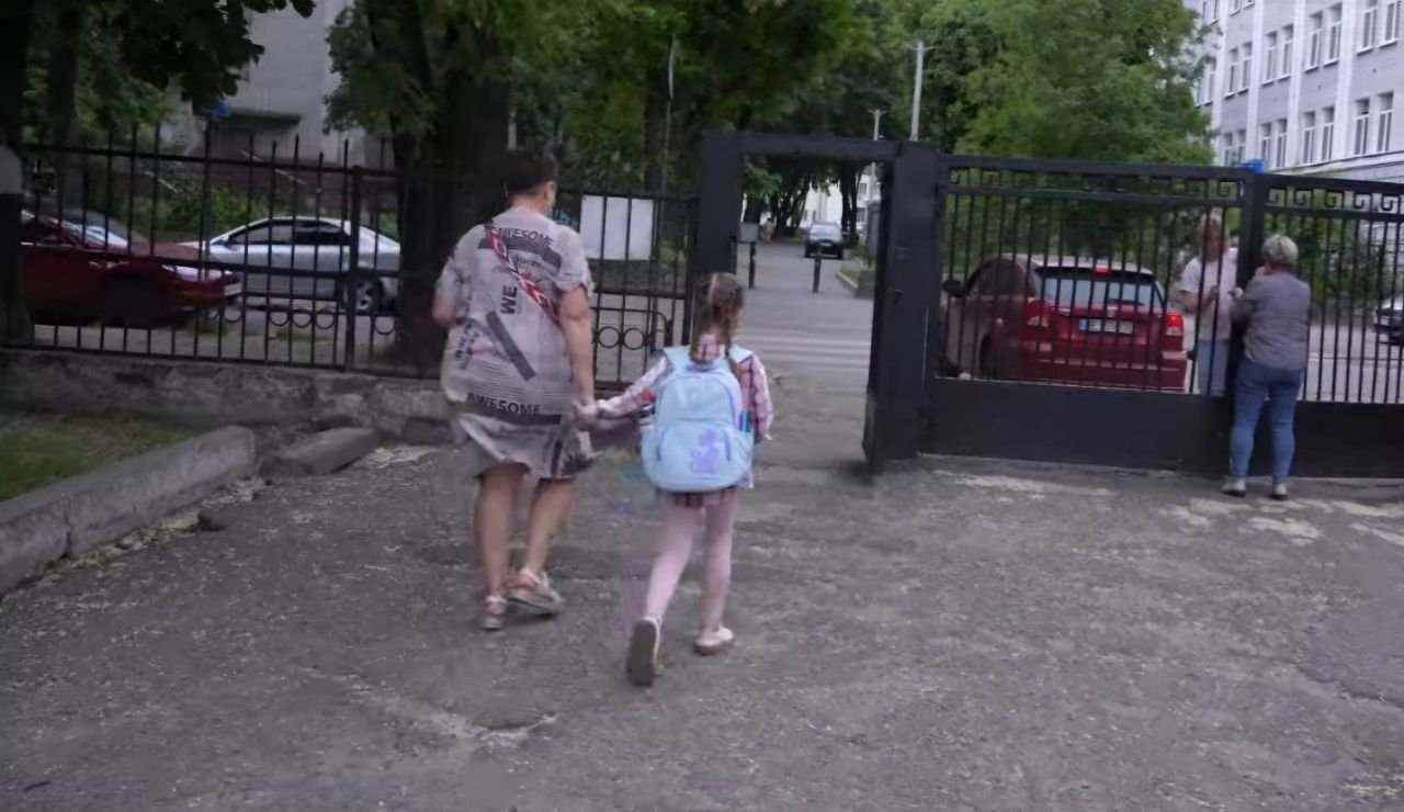  Мати з дитиною виходять з воріт школи